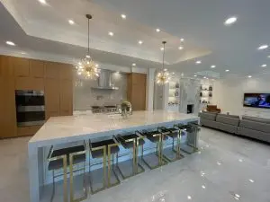 Luxury open-concept kitchen remodel with oversized stone island, wood cabinetry and statement lighting